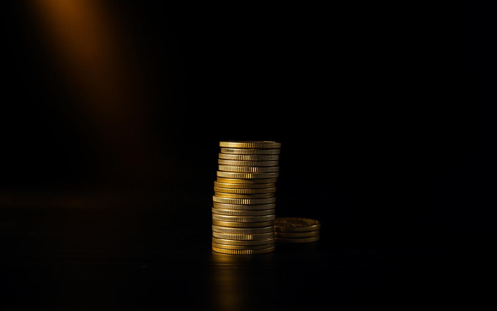 A pyramid stack of gold coins on a dark wooden surface under a single warm gold light